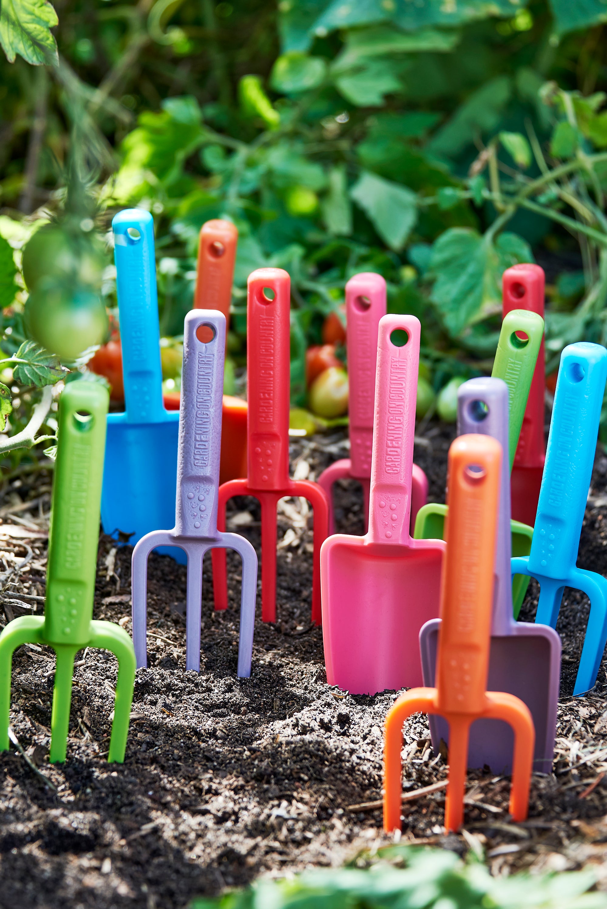 Colorful garden tools made from recycled plastic including shovels and forks on a garden bed.