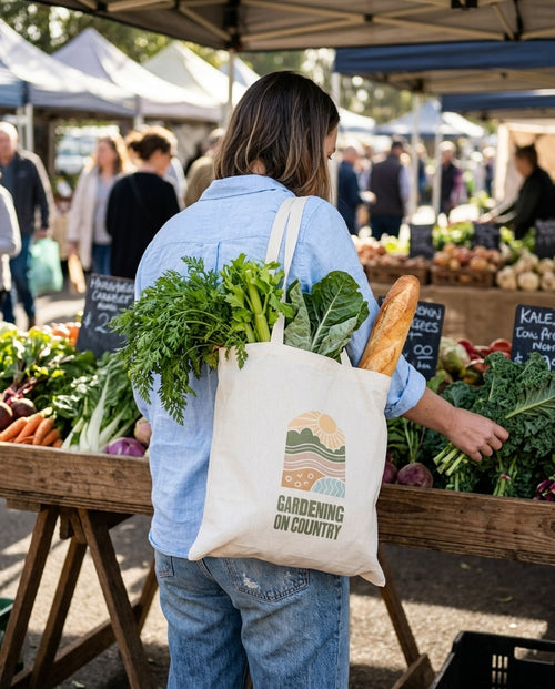 Gardening on Country calico garden bag on a shopper's shoulder at a farmers market, filled with carrots, celery and silverbeet