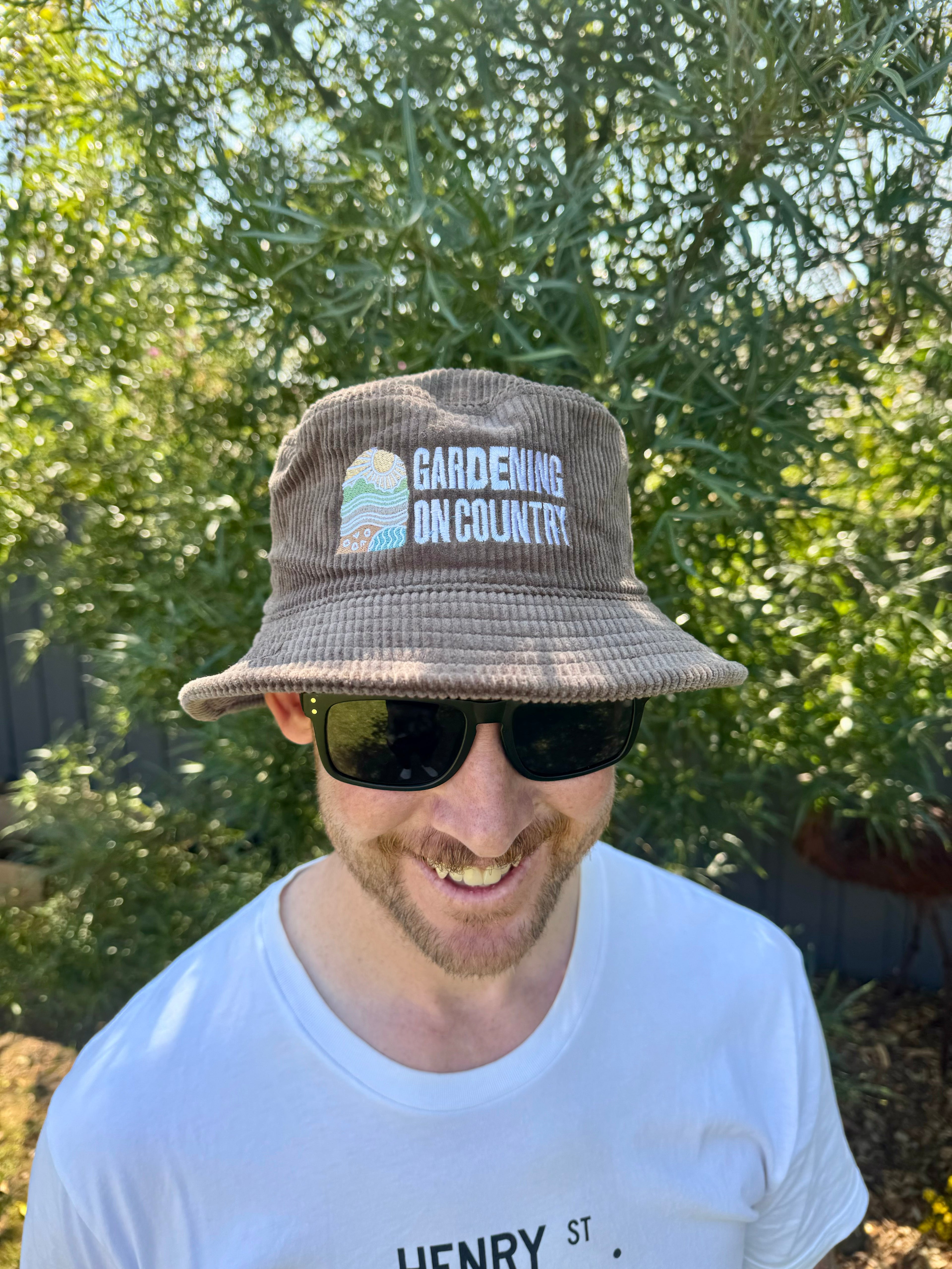 Man wearing brown bucket hat on head with Gardening on Country logo. 
