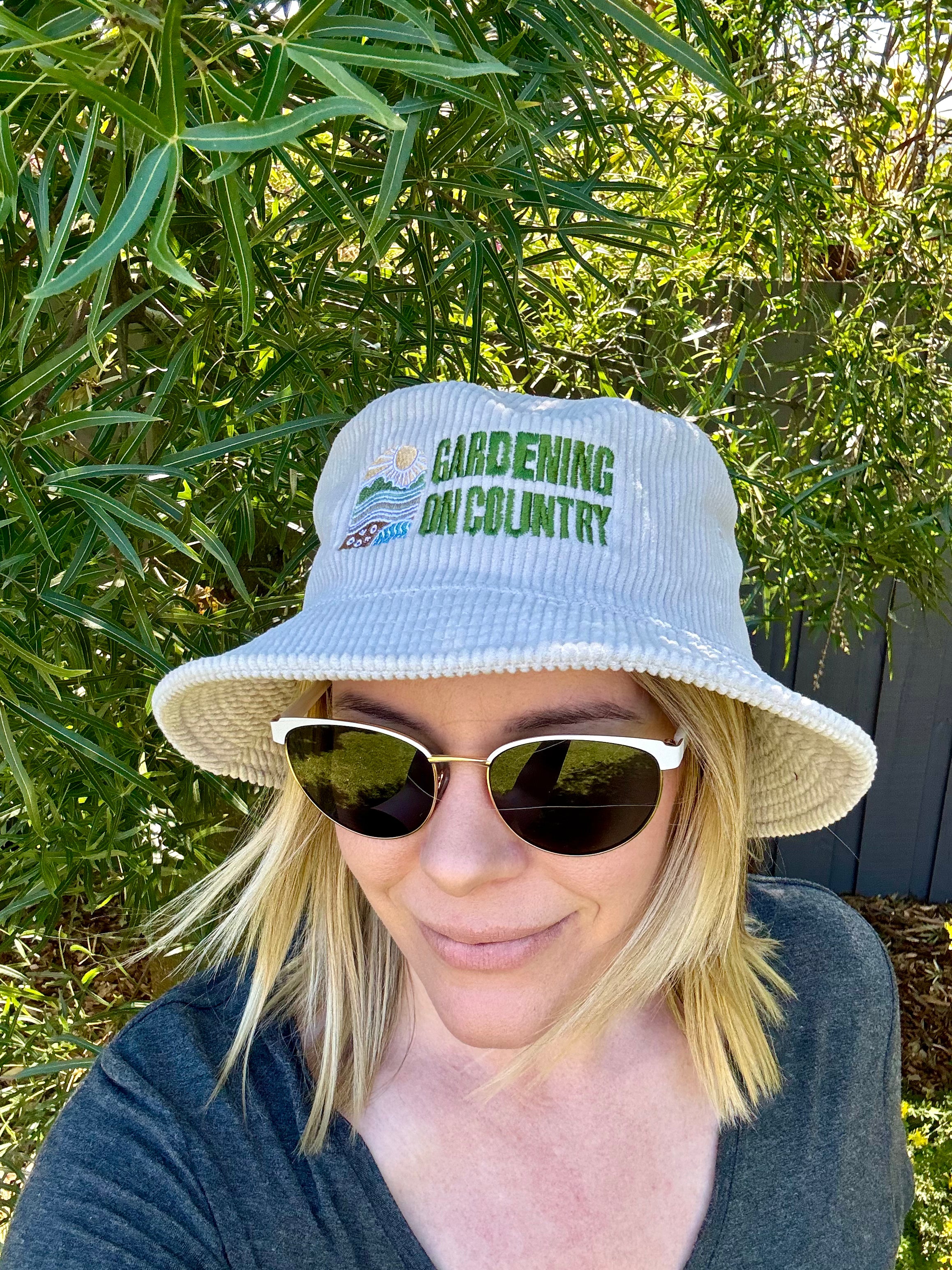 Woman wearing white corduroy bucket hat with Gardening on Country logo