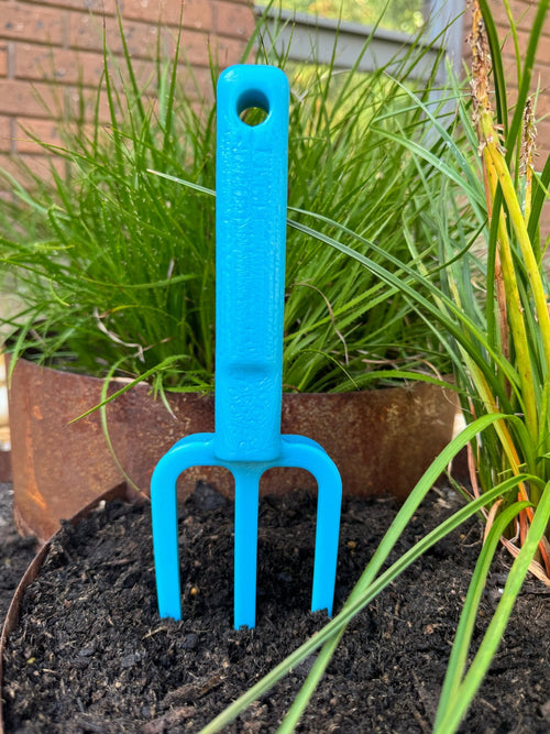 Blue garden fork in soil with plants in the background