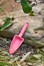 Pink plastic scoop on a natural background with leaves and rocks