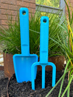 Two blue gardening tools, a shovel and a fork, in a garden setting with plants and soil.
