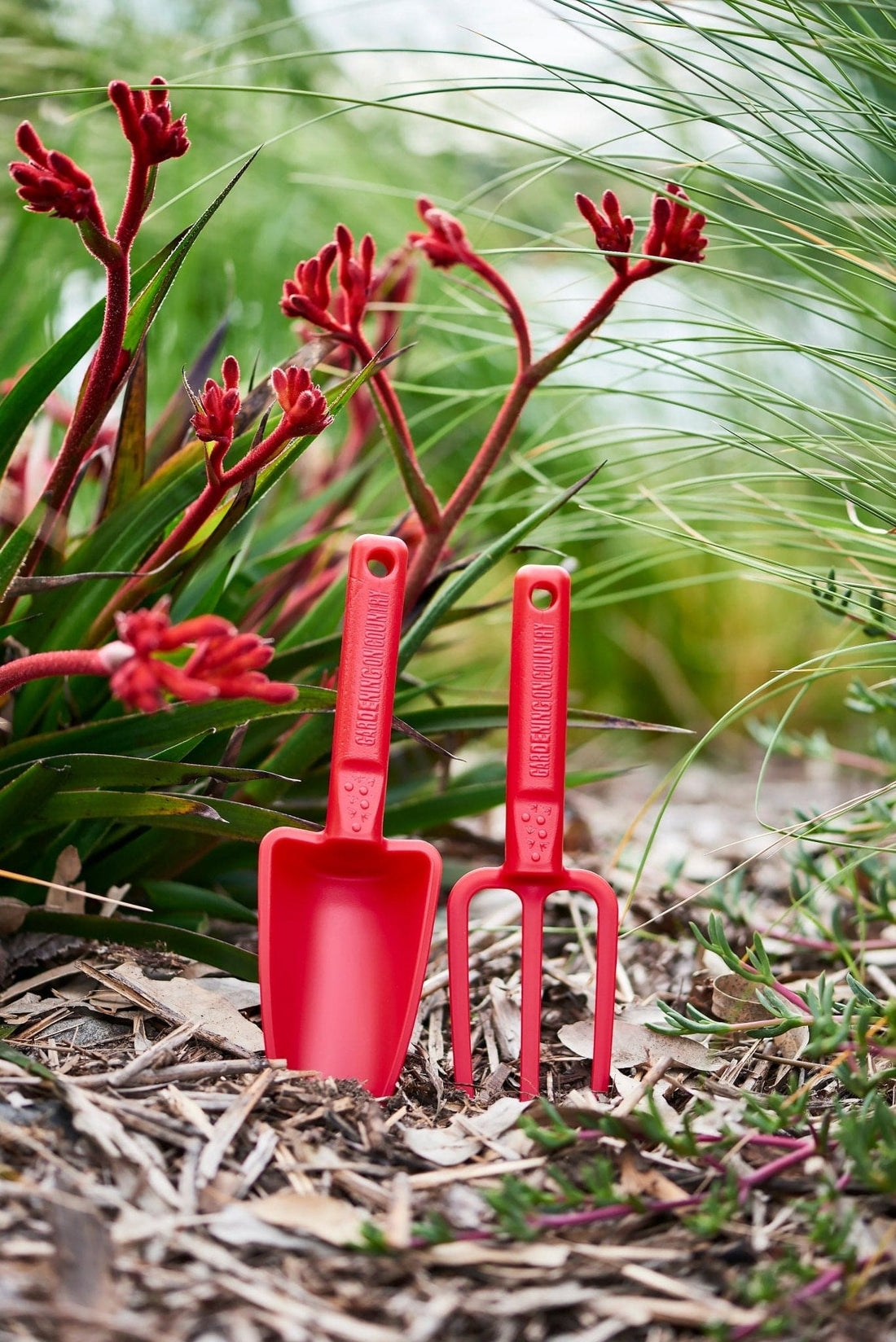 Pink-recycled-plastic-hand-trowel-and-hand-fork-kids-set-laying-against-rock-in-garden