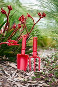 Red-recycled-plastic-hand-trowel-and-hand-fork-kids-set-sitting-in-dirt-garden