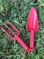 Red-kids-hand-trowel-and-fork-laying-on-succulent-plant