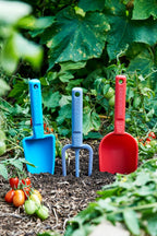 Colorful eco recycled garden tools (shovel, fork, and spade) in a garden setting with plants and tomatoes. Trowel, fork and  scoop.