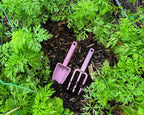 Purple gardening tools in a garden with green plants and soil.